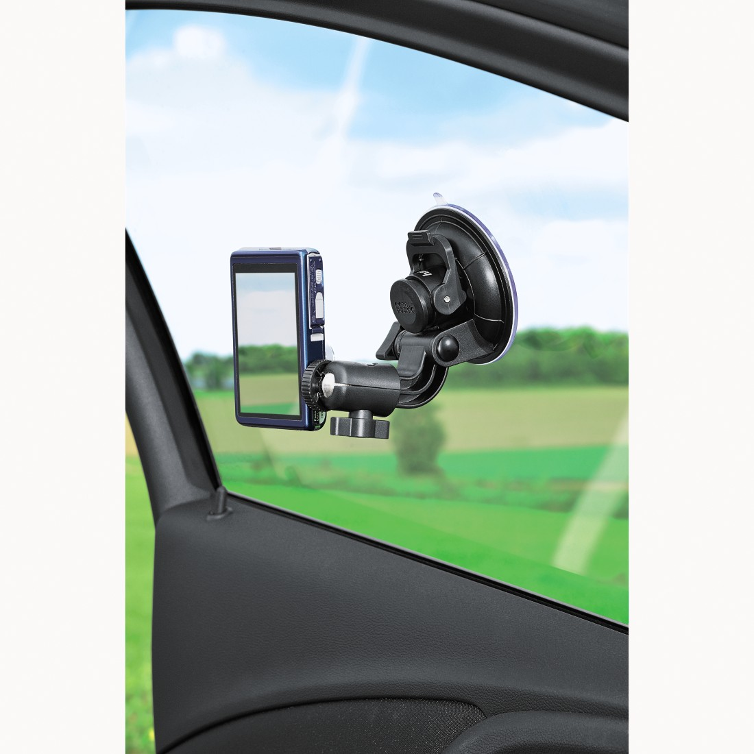 A camera mounted on a car window. Green fields and blue sky visible outside.