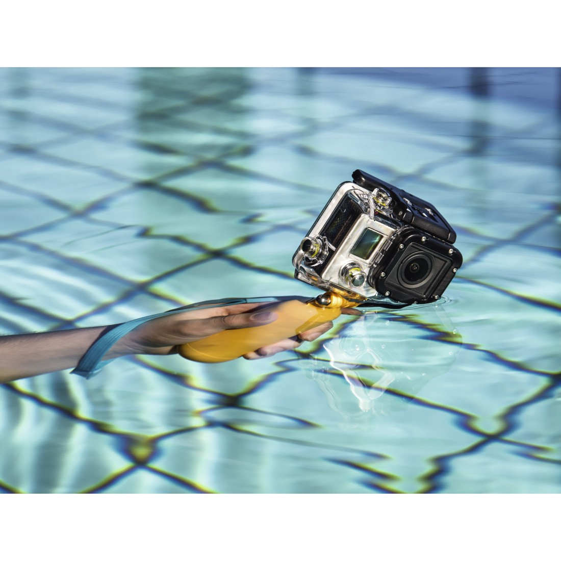 A hand holding a GoPro camera with a yellow float in the water, in a pool.