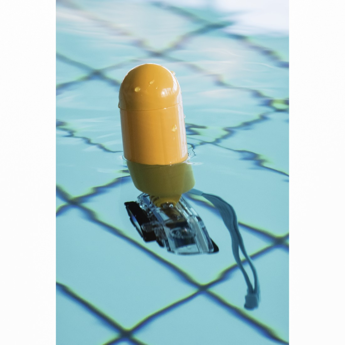 Yellow buoy floating in pool water with a camera attached. Blue tiled pool.