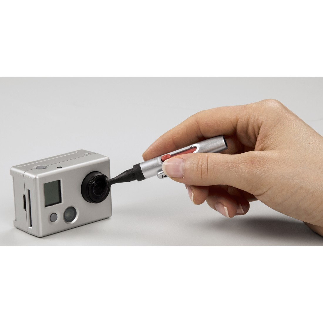 A hand holding a pen cleaning a silver camera lens.