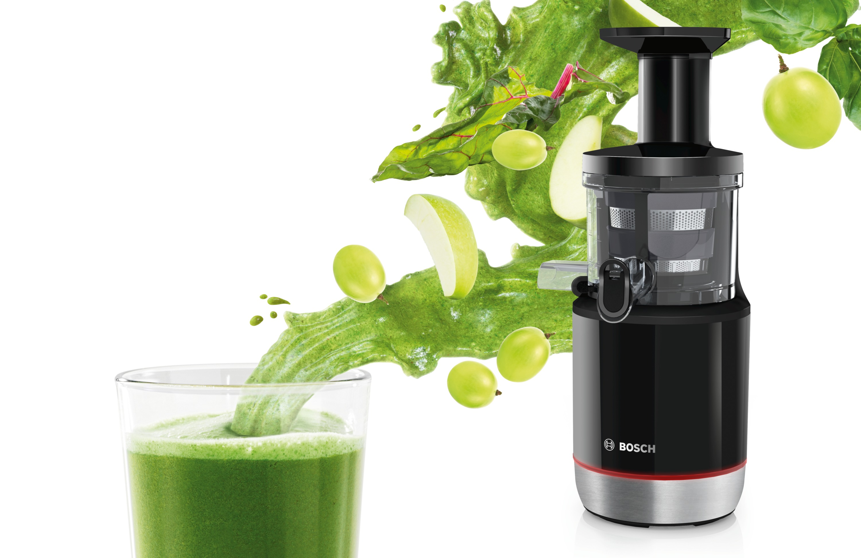 Estrattore di succo con succo verde versato in un bicchiere. Mele verdi e foglie che volano. Sfondo bianco.