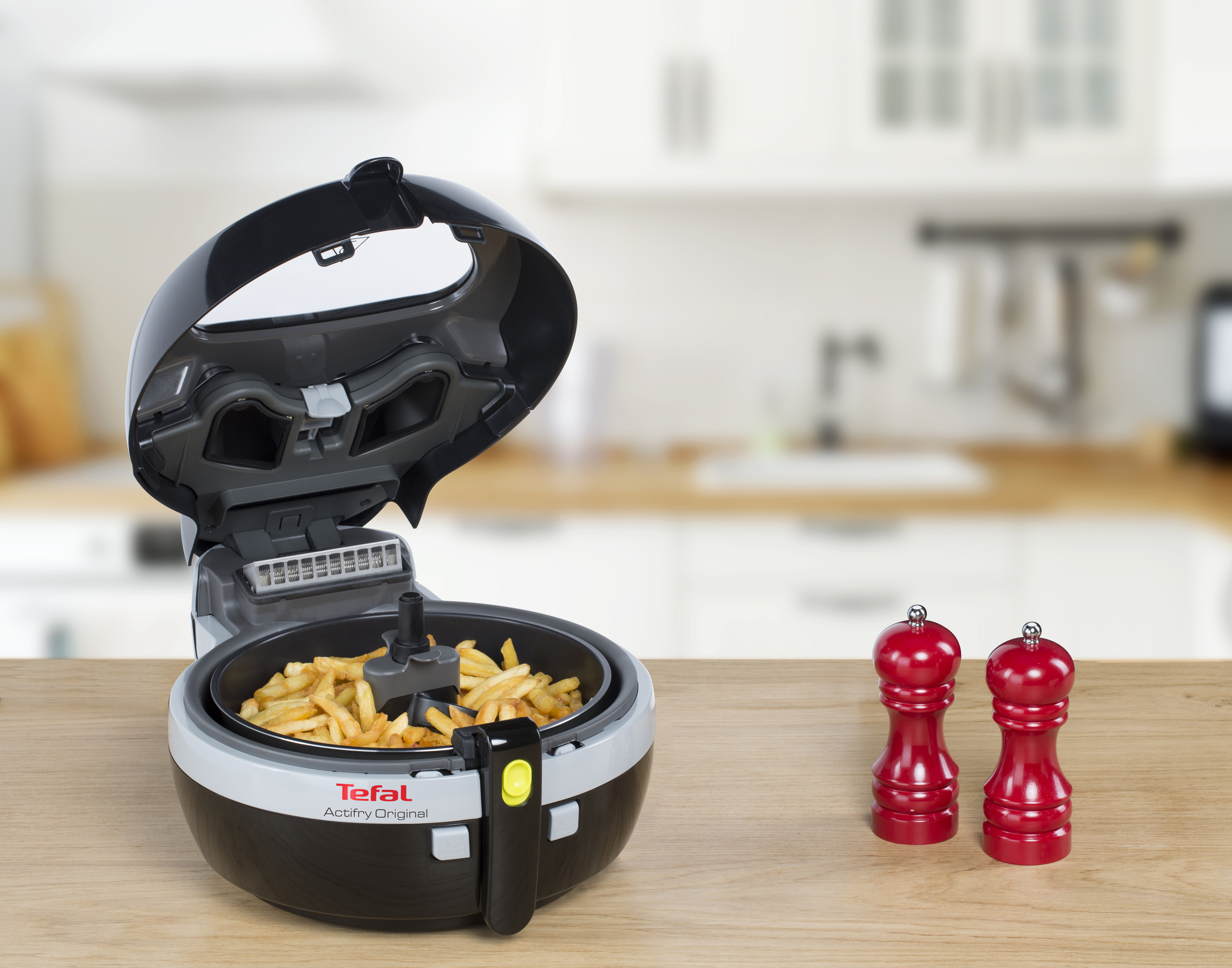 Tefal Actifry, offen. Pommes Frites sind drin. Rote Salz- und Pfefferstreuer stehen daneben.