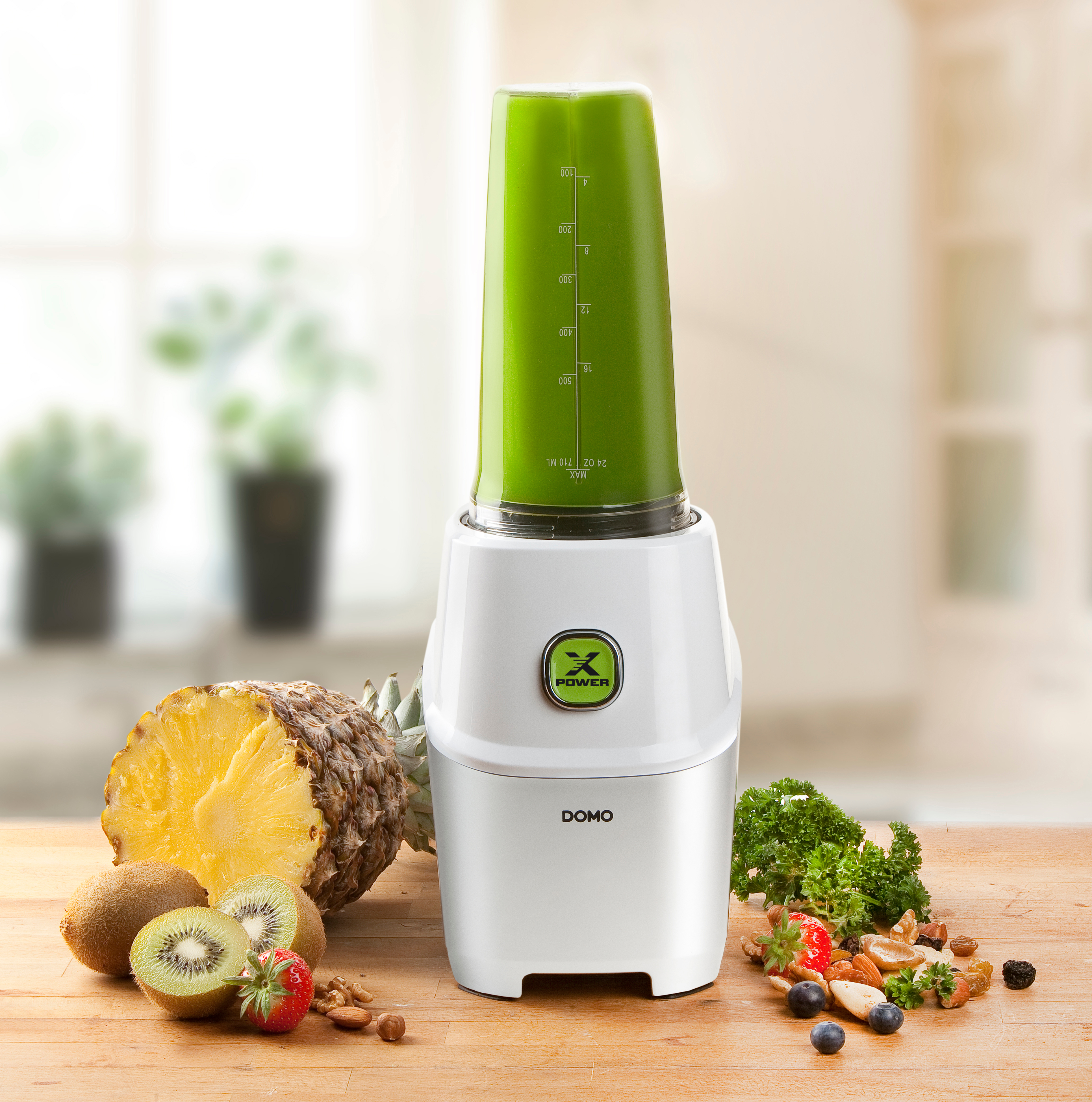 Blender blanc avec smoothie vert à l'intérieur et des fruits autour. Il y a de l'ananas et du kiwi.