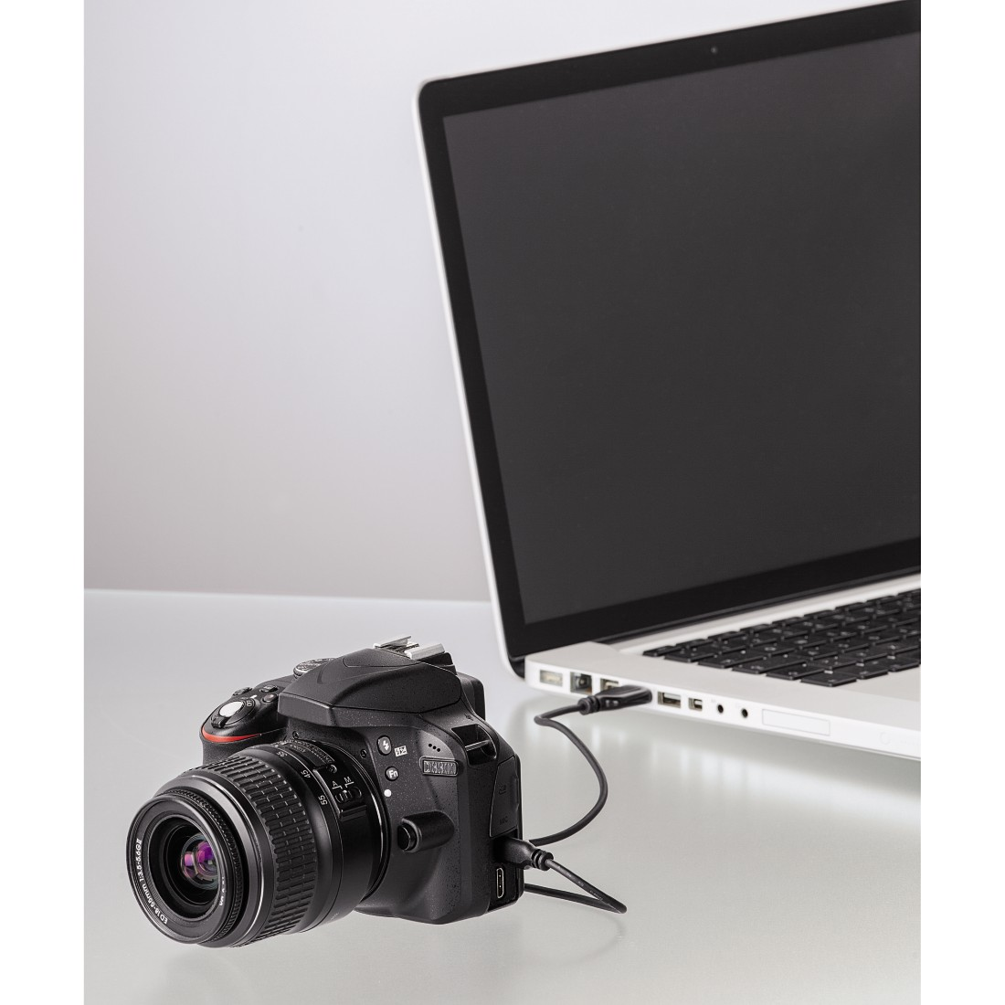 Een zwarte DSLR-camera aangesloten op een laptop via een USB-kabel.