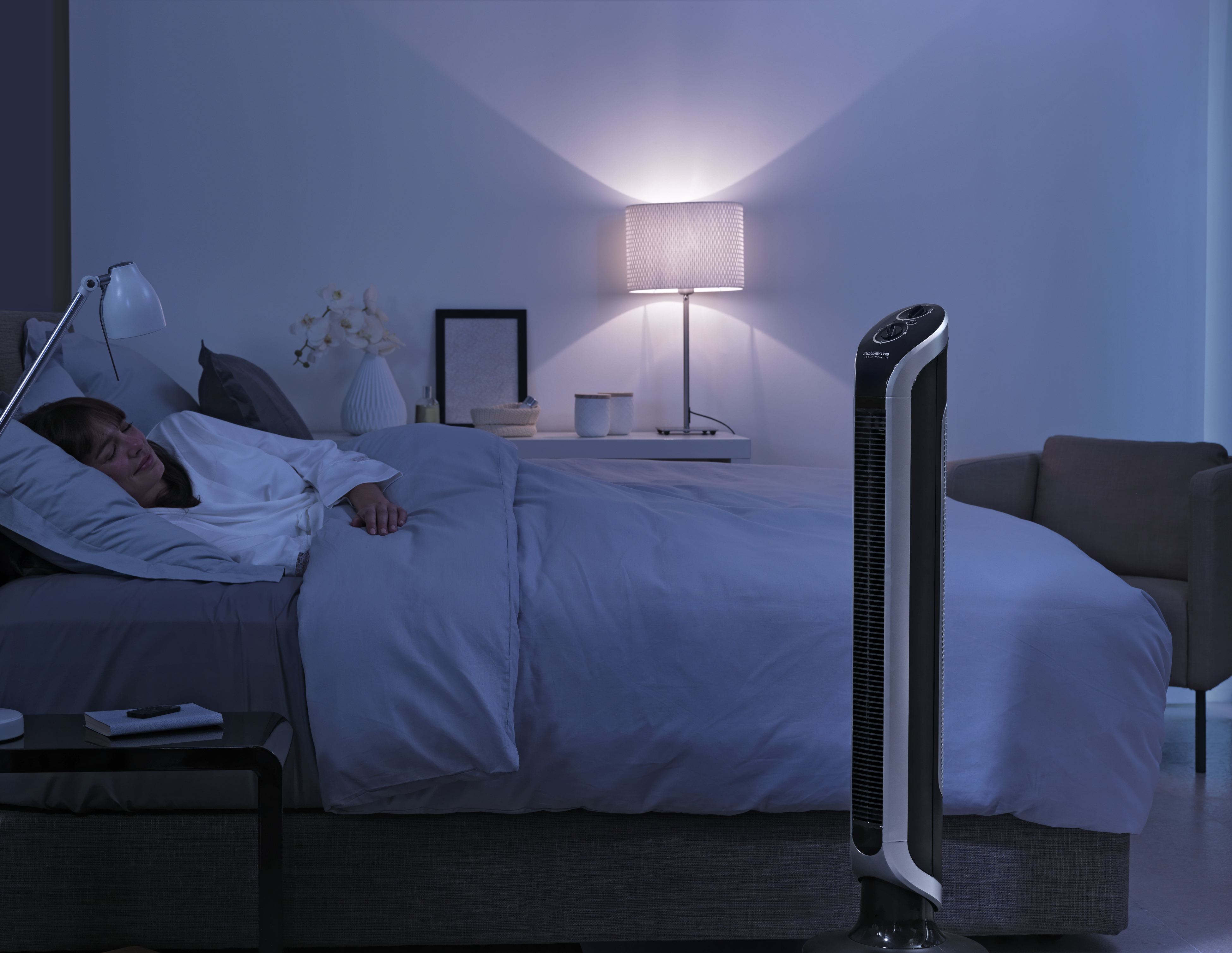 Scène de chambre à coucher la nuit. Une femme dort dans le lit. Un ventilateur à côté.