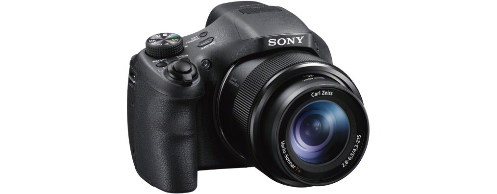 Schwarze Sony Kamera mit Objektiv. Carl Zeiss Objektiv sichtbar. Sony Logo oben. Weißer Hintergrund.