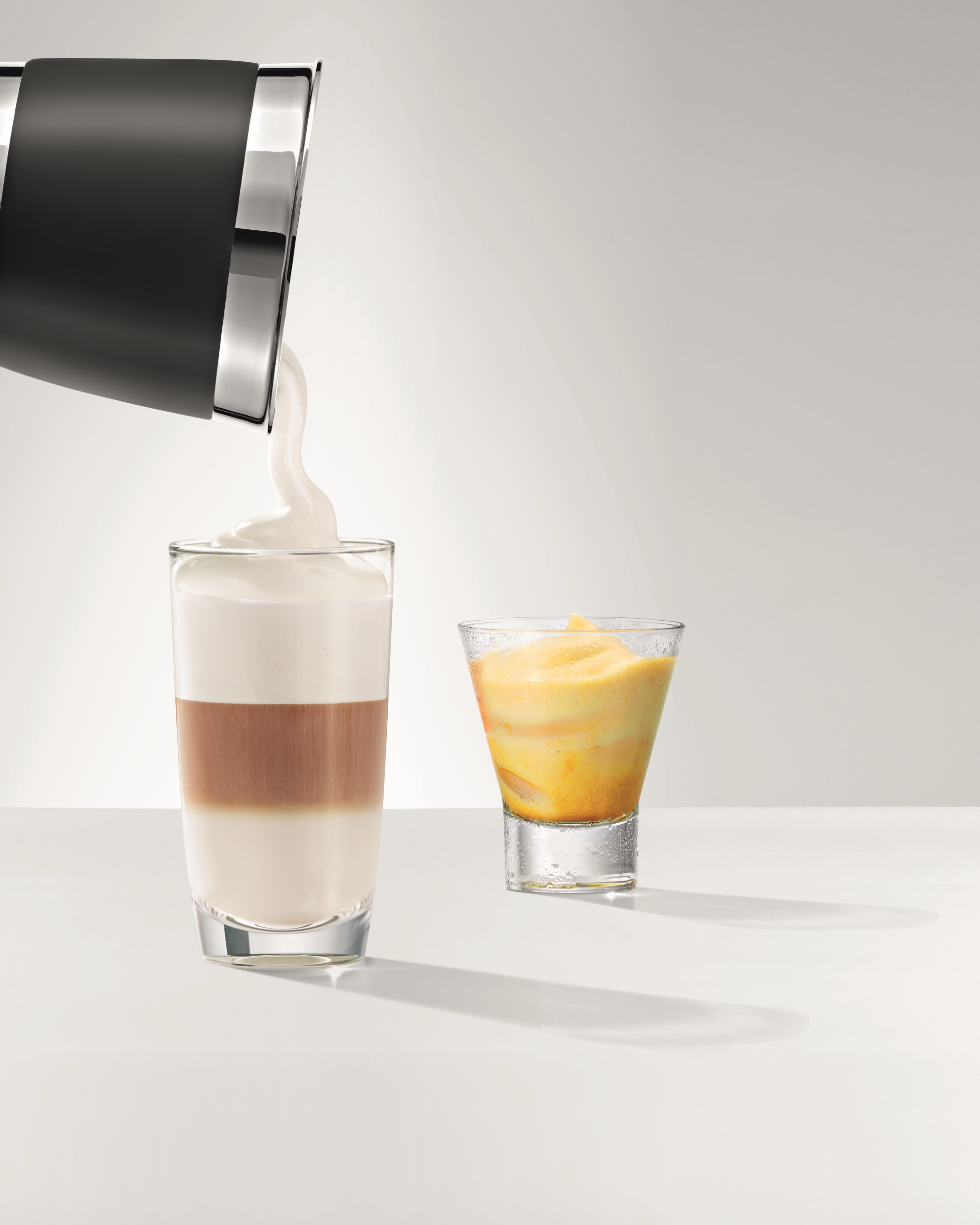 Milch wird in einen geschichteten Latte und ein gelbes Mixgetränk in ein Glas gegossen.