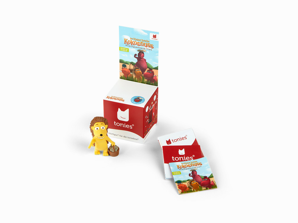 Ein Löwenspielzeug und ein Büchersatz vor einer Ausstellungsbox. Box und Bücher haben Rot- und Weißtöne.