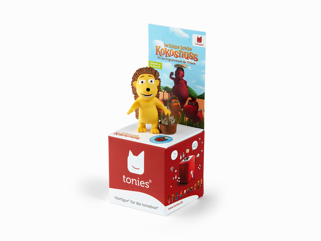 Ein kleines Spielzeug eines gelben Drachen mit einer Box und dem Text 'die kleine Kokosnuss'.