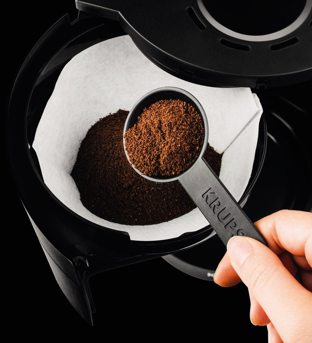 Coffee grounds being scooped into a filter in a coffee maker.