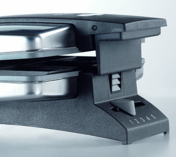 A raclette grill közelképe 1-5-ig számozott tárcsával és két fémtálcával.