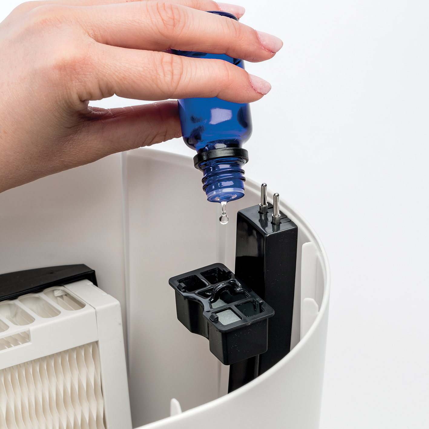 Eine Hand gießt blaue Flüssigkeit in einen weißen Behälter. Die Flüssigkeit stammt aus einer blauen Flasche.