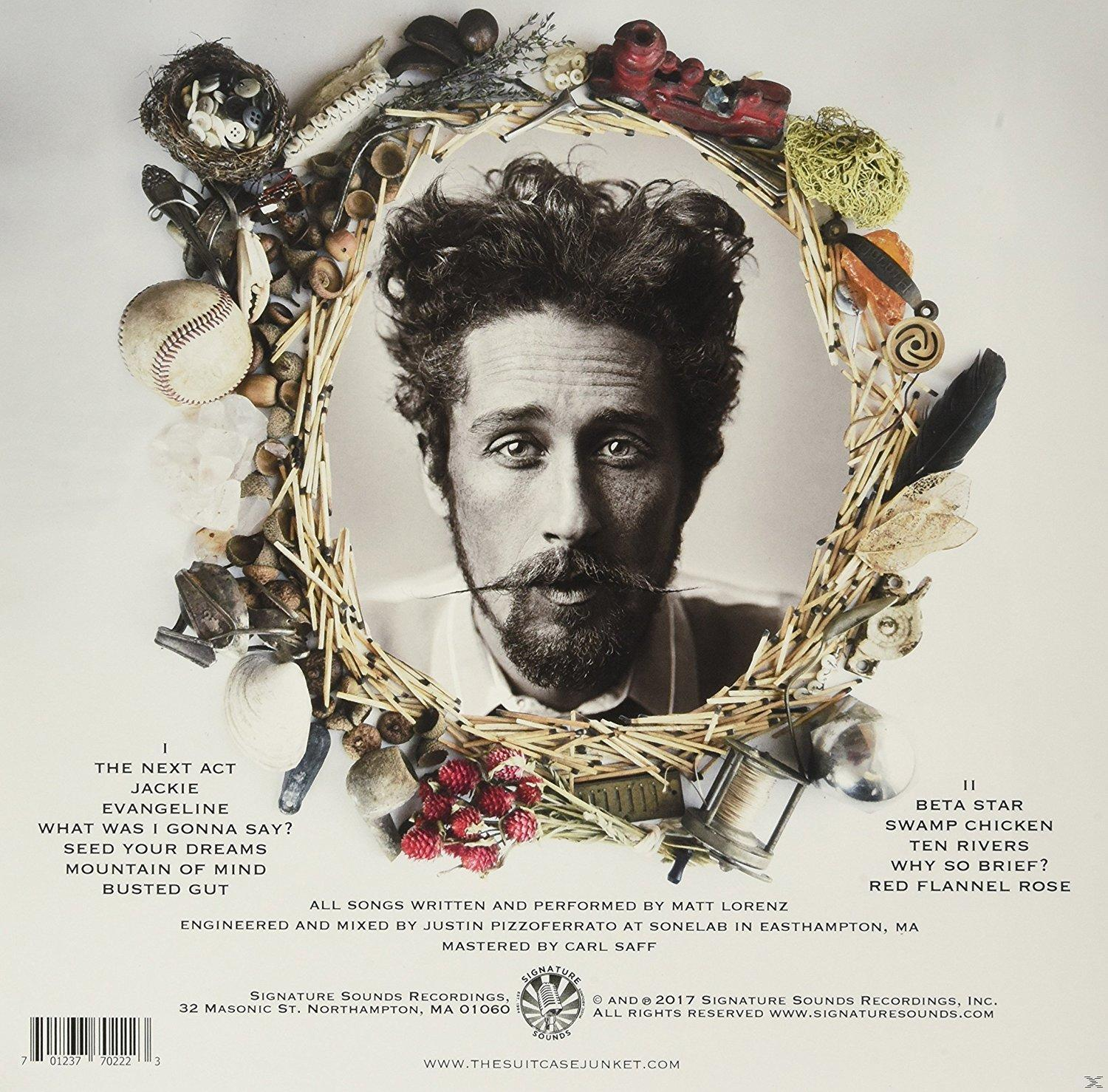 CD-Cover mit einem Porträt eines Mannes in einem Kranz aus Objekten wie einem Vogelnest, Blumen und Werkzeugen.