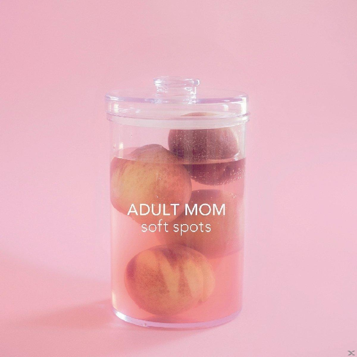 Klares Glas mit Pfirsichen in rosa Flüssigkeit, Text: ADULT MOM soft spots, auf rosa Hintergrund.