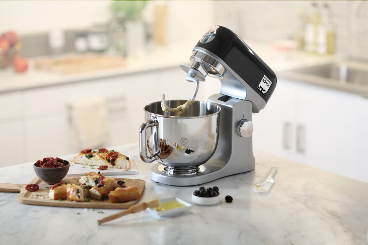 Keuken met een zilveren en zwarte standmixer, brood, olijven en andere voedingsmiddelen.