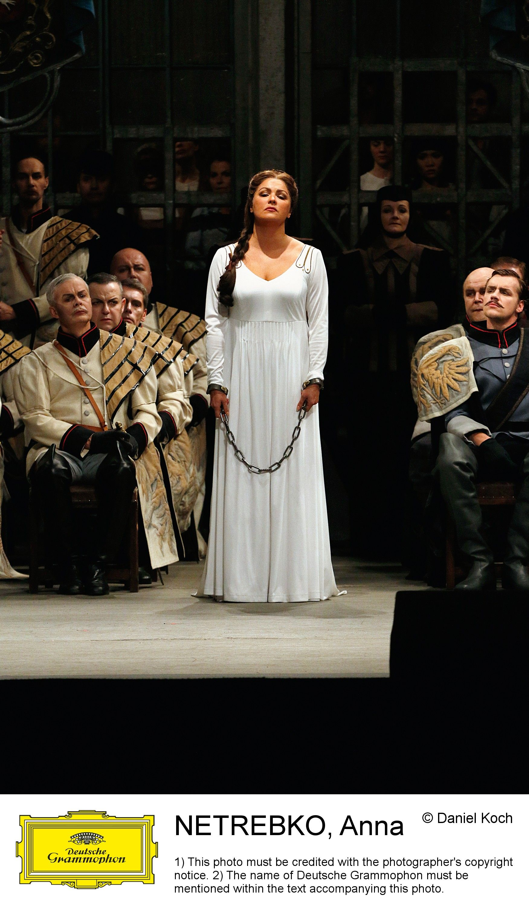 Opernsängerin in weißem Kleid, angekettet, mit anderen in historischer Kleidung.