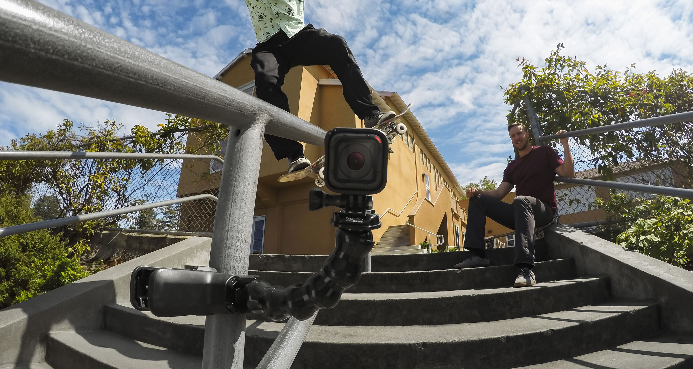 Egy gördeszkás a korláton egy GoPro kamerával. Egy másik személy a lépcsőkről nézi.