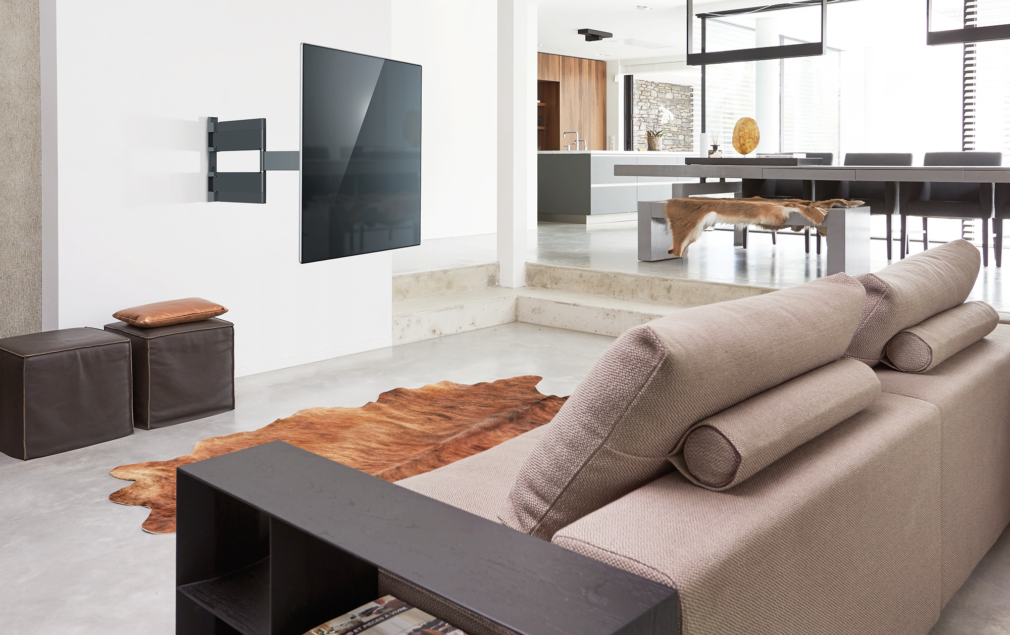 Woonkamer met tv aan de muur, bank, kleed en uitzicht op de keuken.