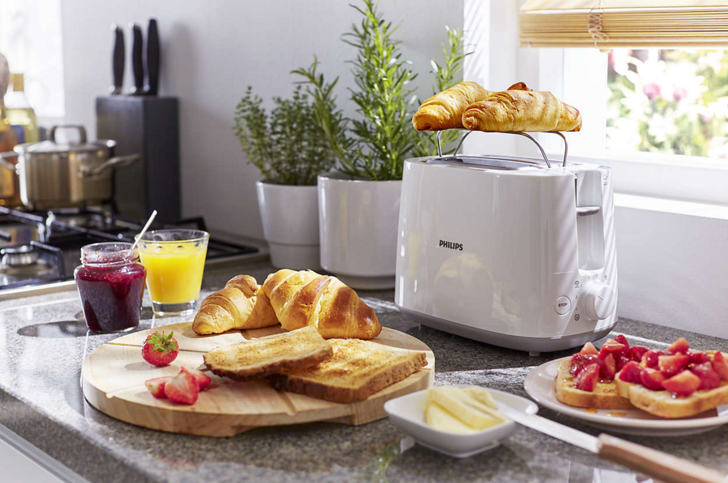 Ontbijt. Broodrooster met croissants erop, sap, jam, aardbeien, toast en boter.