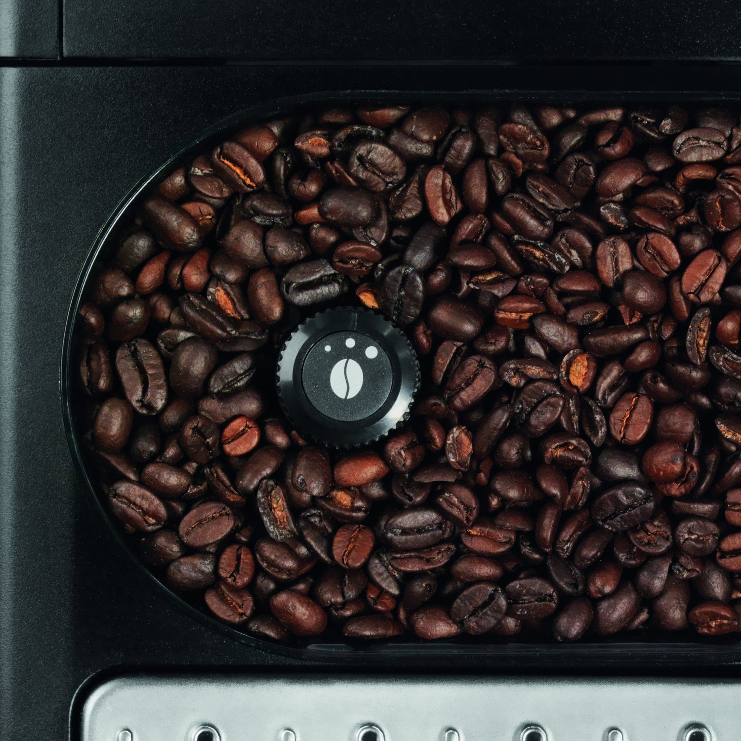 Nahaufnahme von Kaffeebohnen in einem schwarzen Behälter. Ein Knopf ist sichtbar. Die Bohnen sind braun.