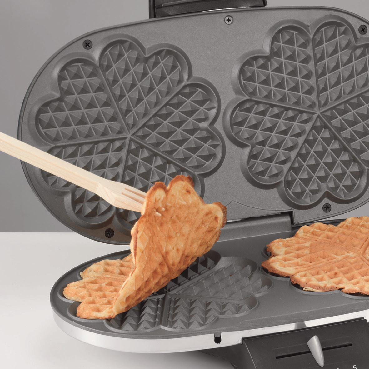 Waffeleisen mit einer entnommenen Waffel. Waffeln haben herzförmige Muster.