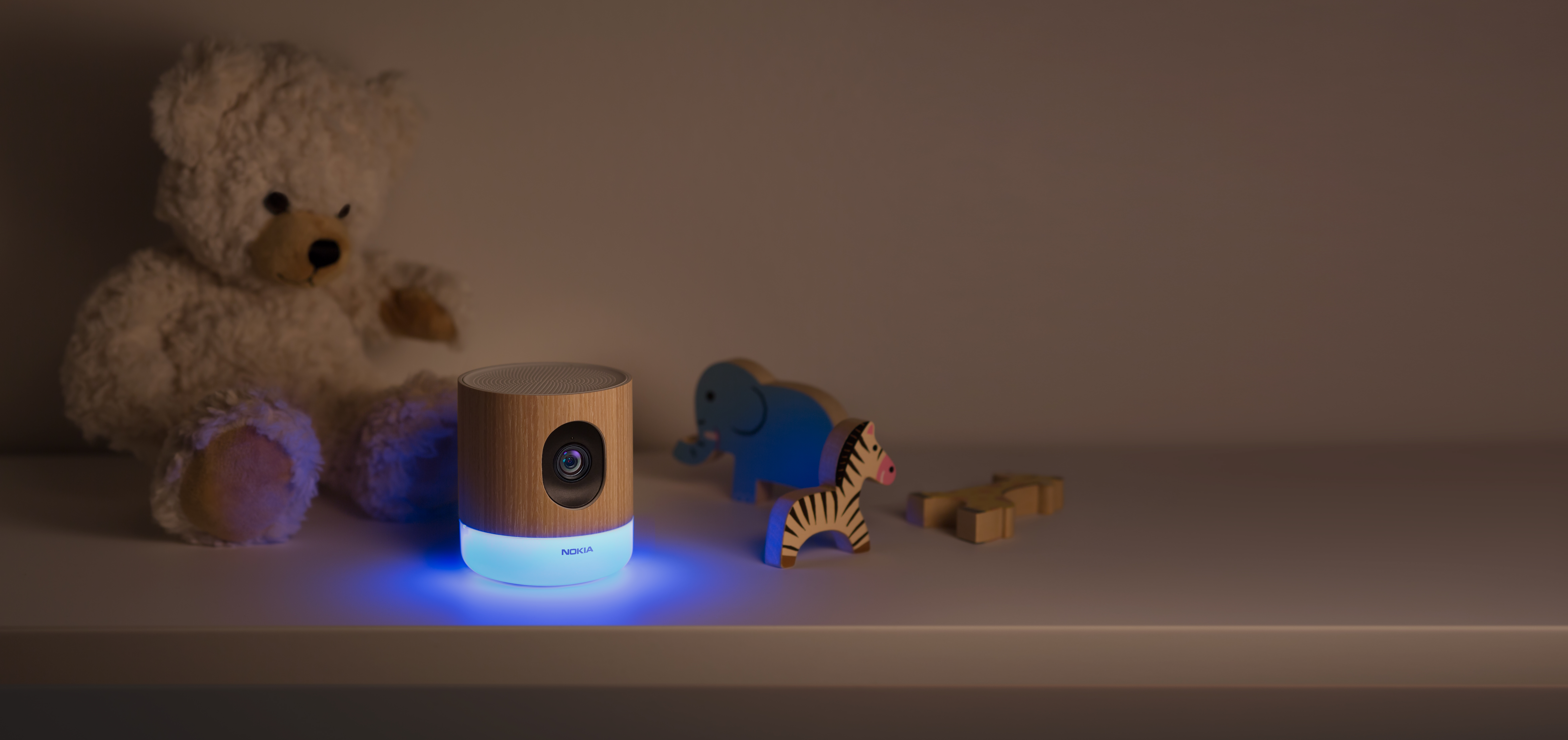Ein Holzprojektor, Teddybär, Spielzeugelefant und Zebra auf einem Regal. Blaues Licht geht von der Projektorbasis aus.