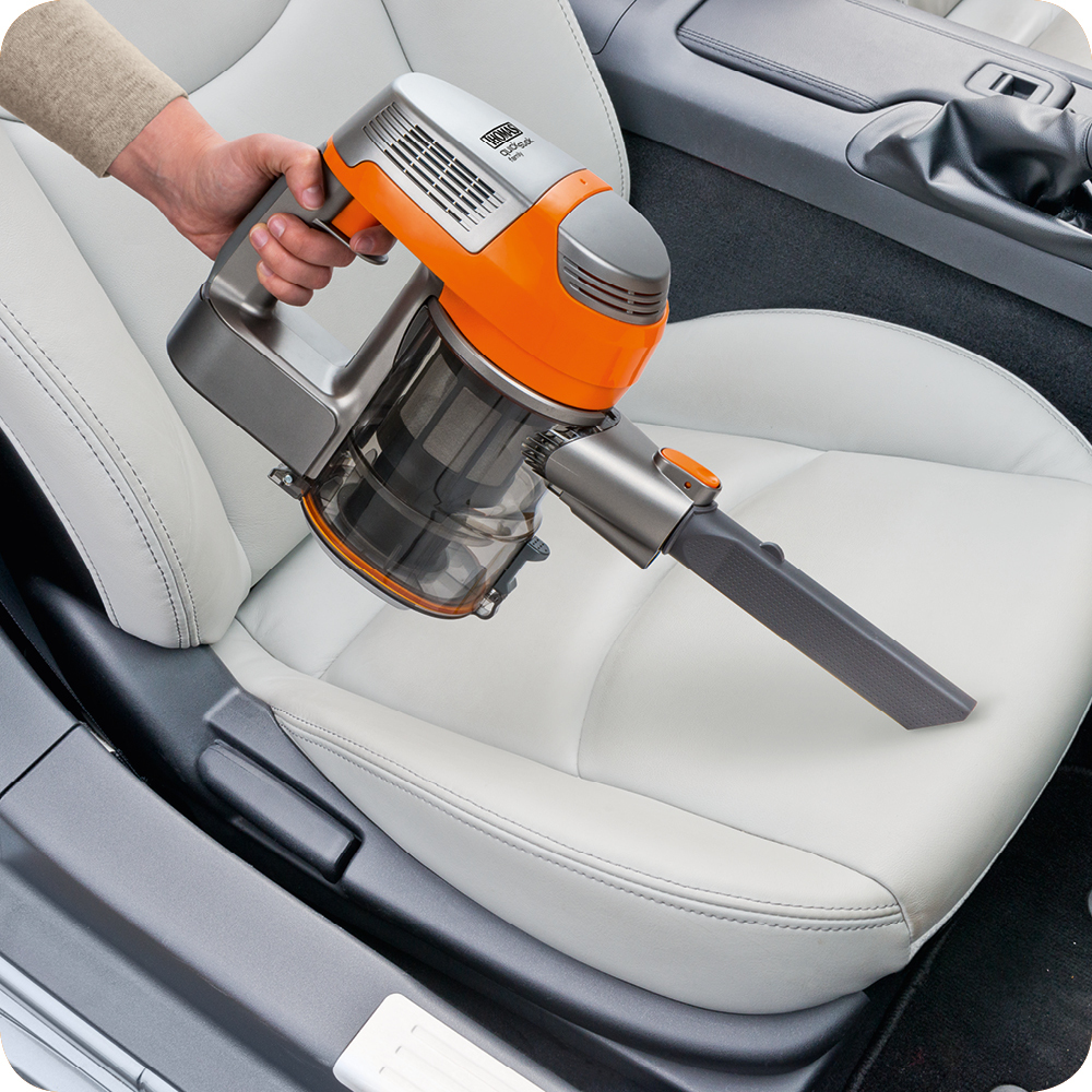Eine Person benutzt einen orange-grauen Handstaubsauger auf einem weißen Autositz.