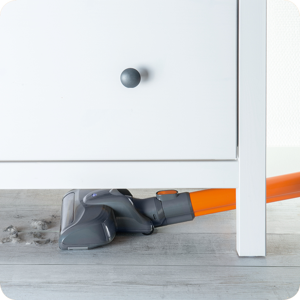 Ein Staubsauger reinigt einen Boden. Es gibt einen weißen Schrank und Haare auf dem Boden.