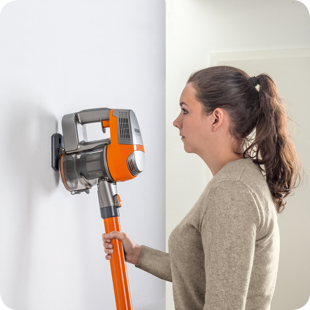 Frau, die einen Stabstaubsauger an einer weißen Wand benutzt.