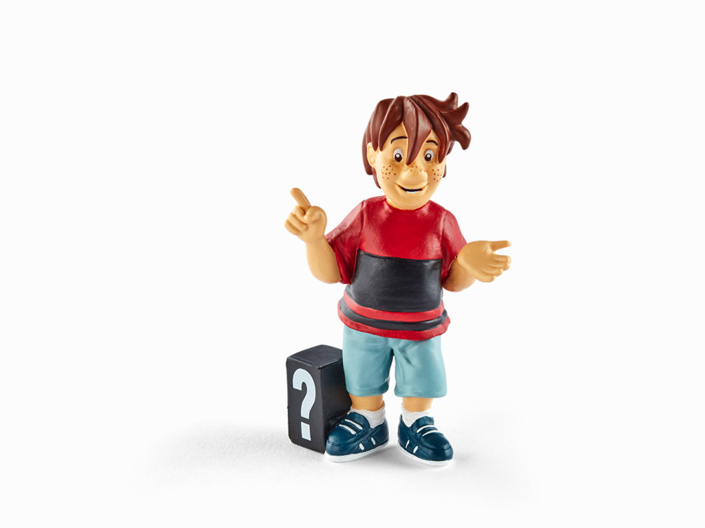 Eine Figur eines Jungen mit braunen Haaren und Sommersprossen, der ein rotes Hemd und blaue Shorts trägt, zeigt. Eine schwarze Box mit einem Fragezeichen.