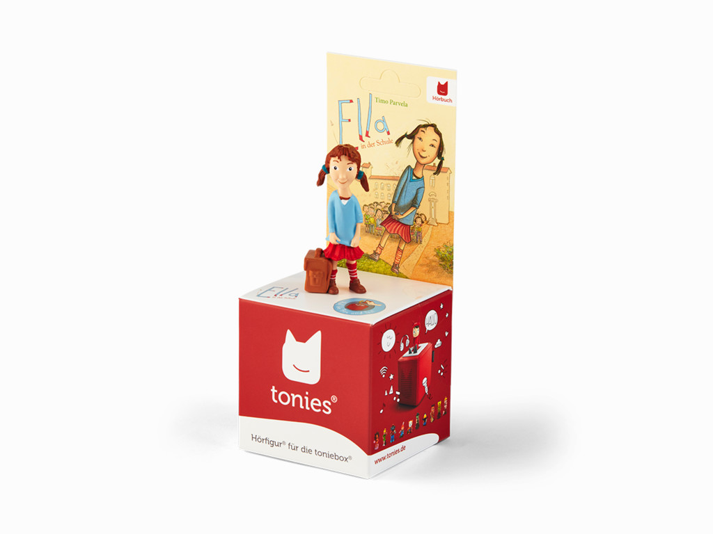 Eine Tonies-Spielfigur eines Mädchens mit einem Buch, auf einer roten Box, auf weißer Oberfläche.