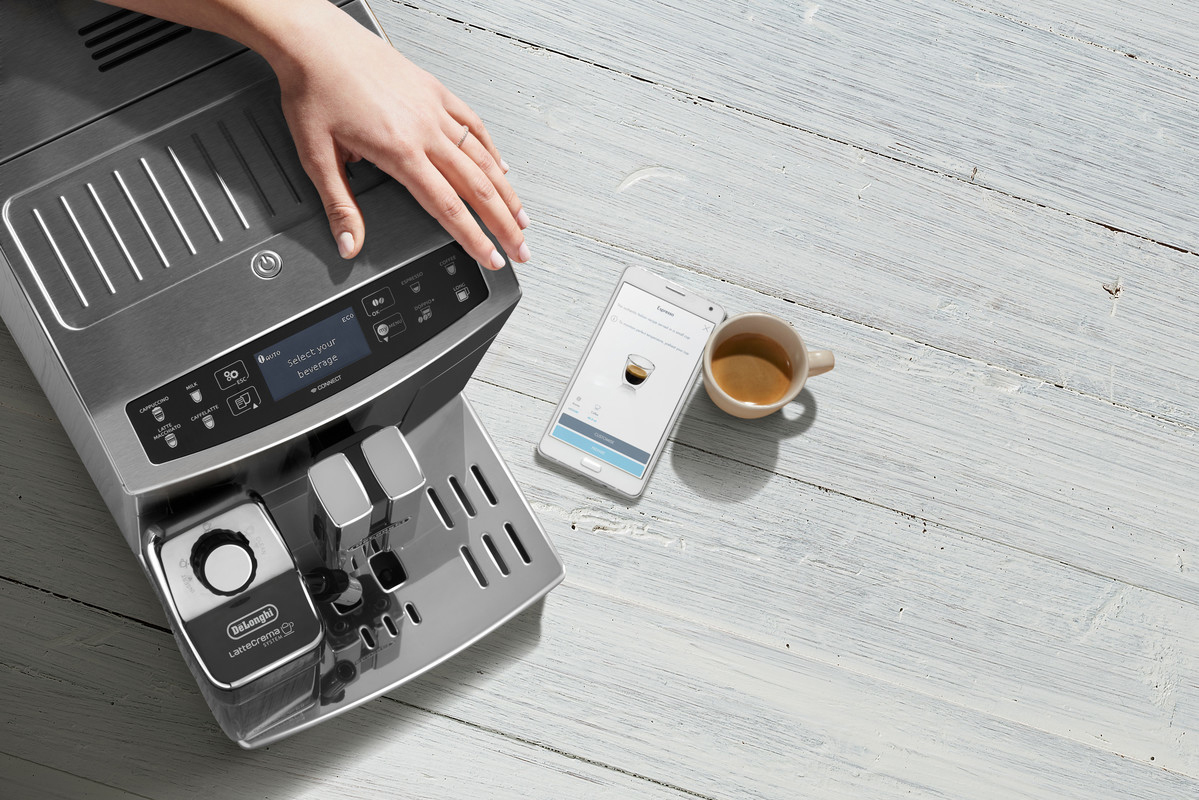 Eine Kaffeemaschine, ein Telefon mit einer Kaffee-App und eine Tasse Kaffee auf Holz.