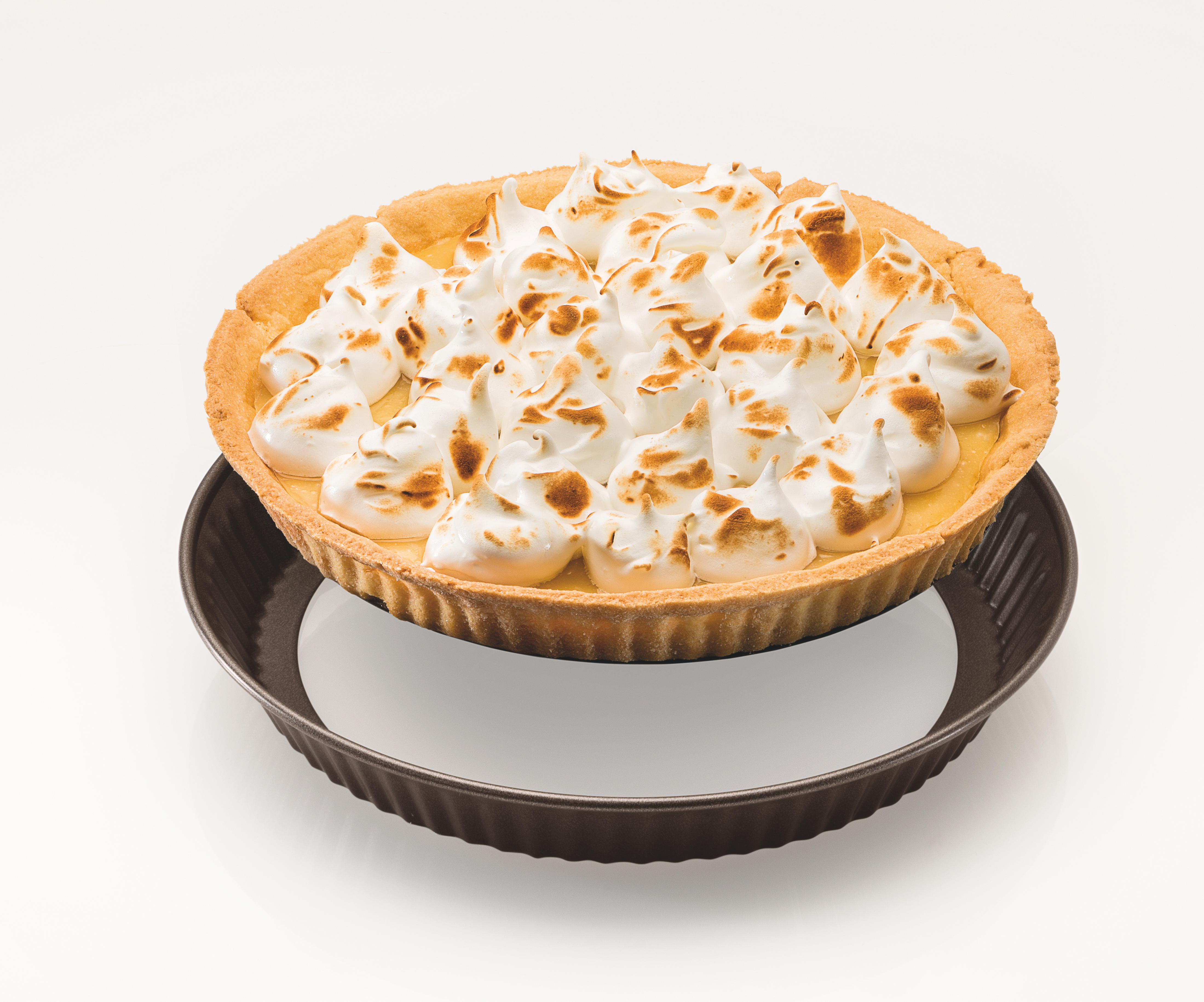 Ein Zitronenbaiser-Kuchen in einer dunkelbraunen Kuchenform, auf weißer Oberfläche.