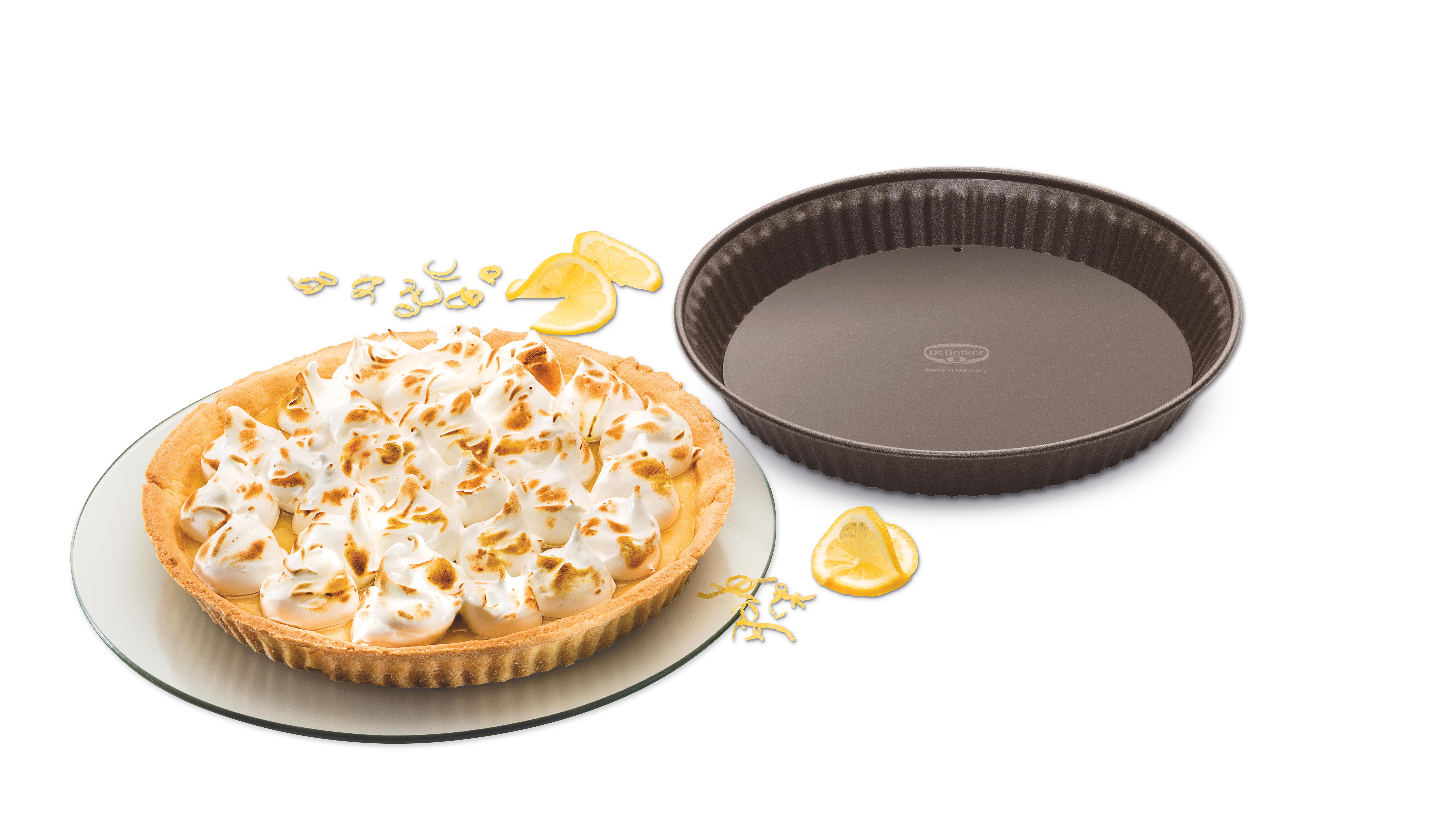 Zitronenbaiser-Torte auf einem Glasteller. Eine braune Kuchenform daneben. Zitronenscheiben und Schale sind vorhanden.
