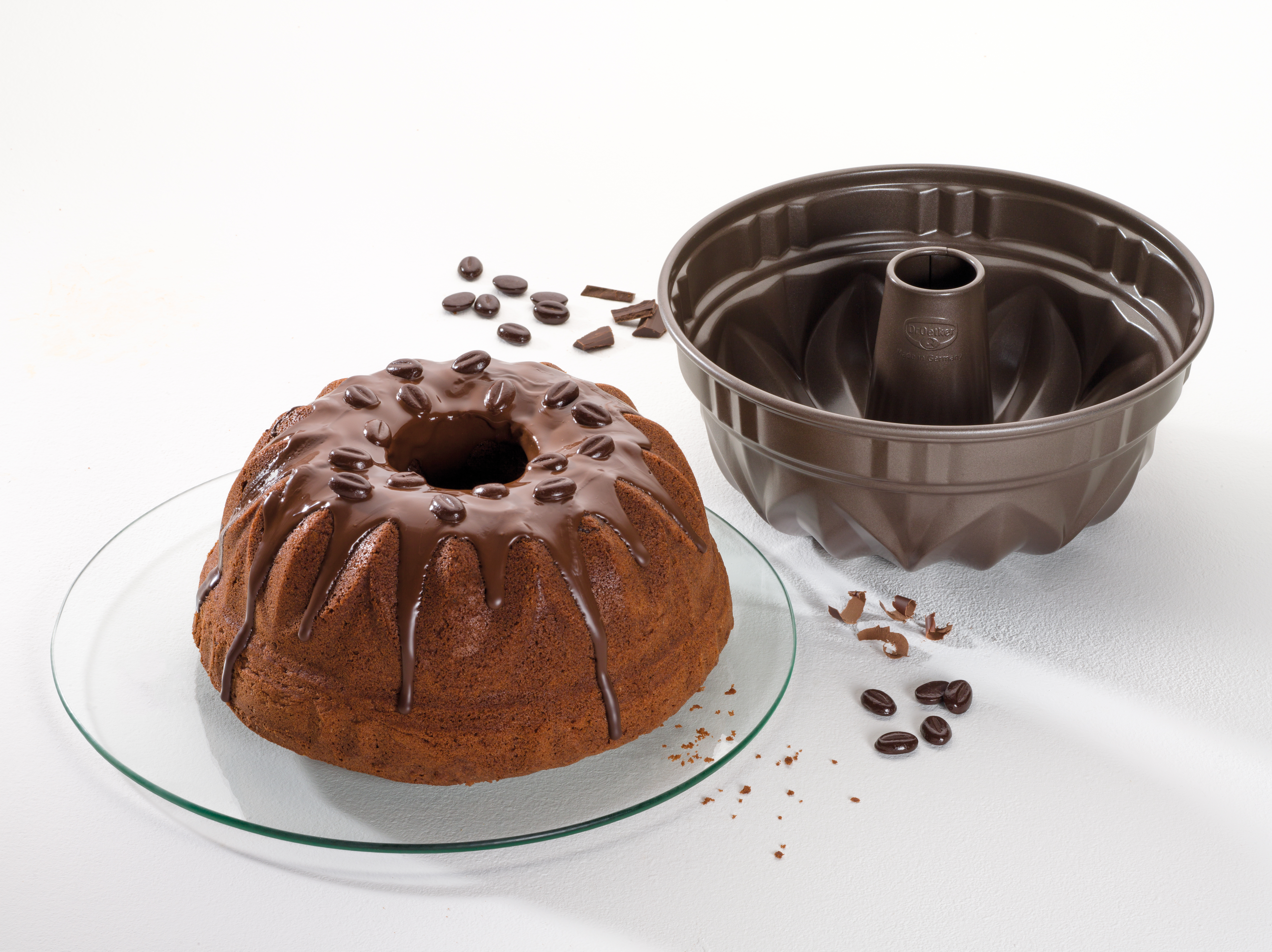 Schokoladenkuchen mit Schokosauce auf einem Glasteller, neben einer Gugelhupf-Form mit Kaffeebohnen.