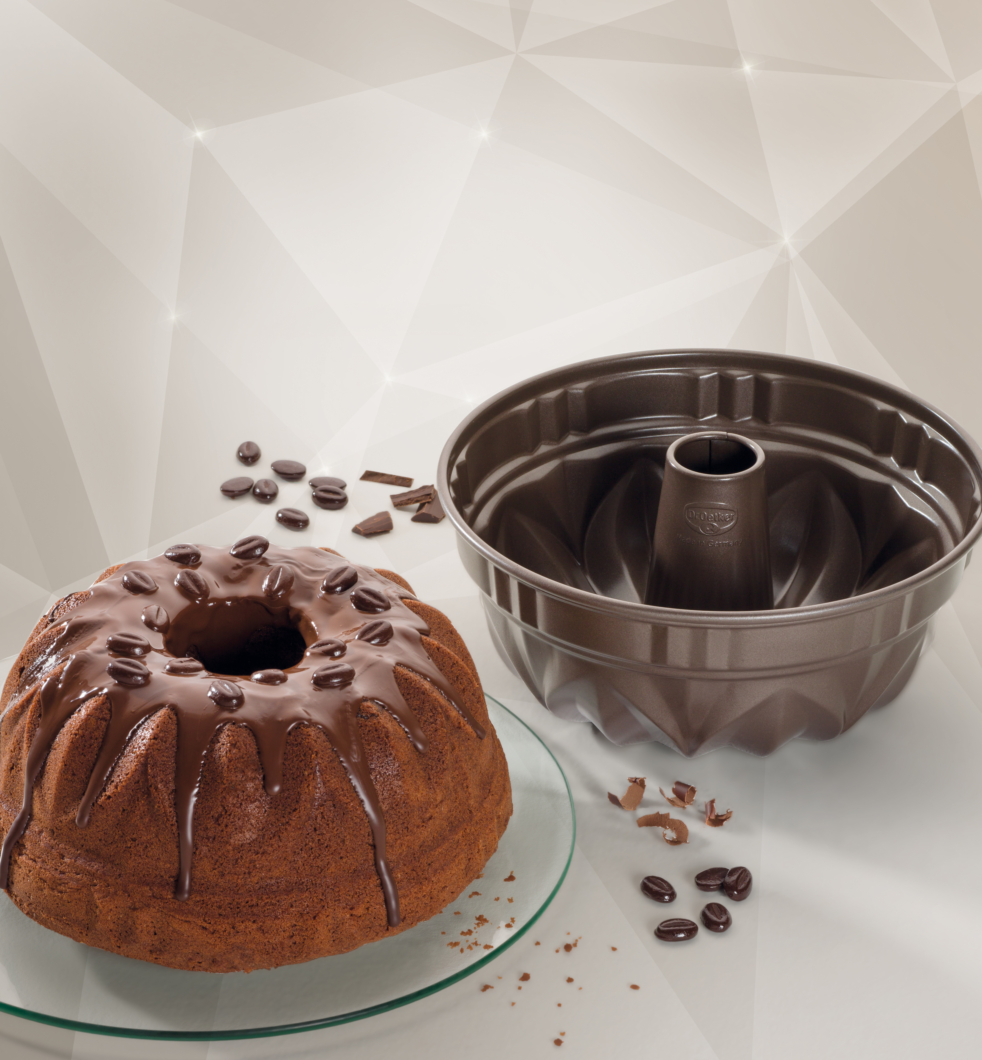 Gugelhupf mit Schokoladenglasur und Kaffeebohnen auf einem Glasteller. Daneben eine Gugelhupfform.
