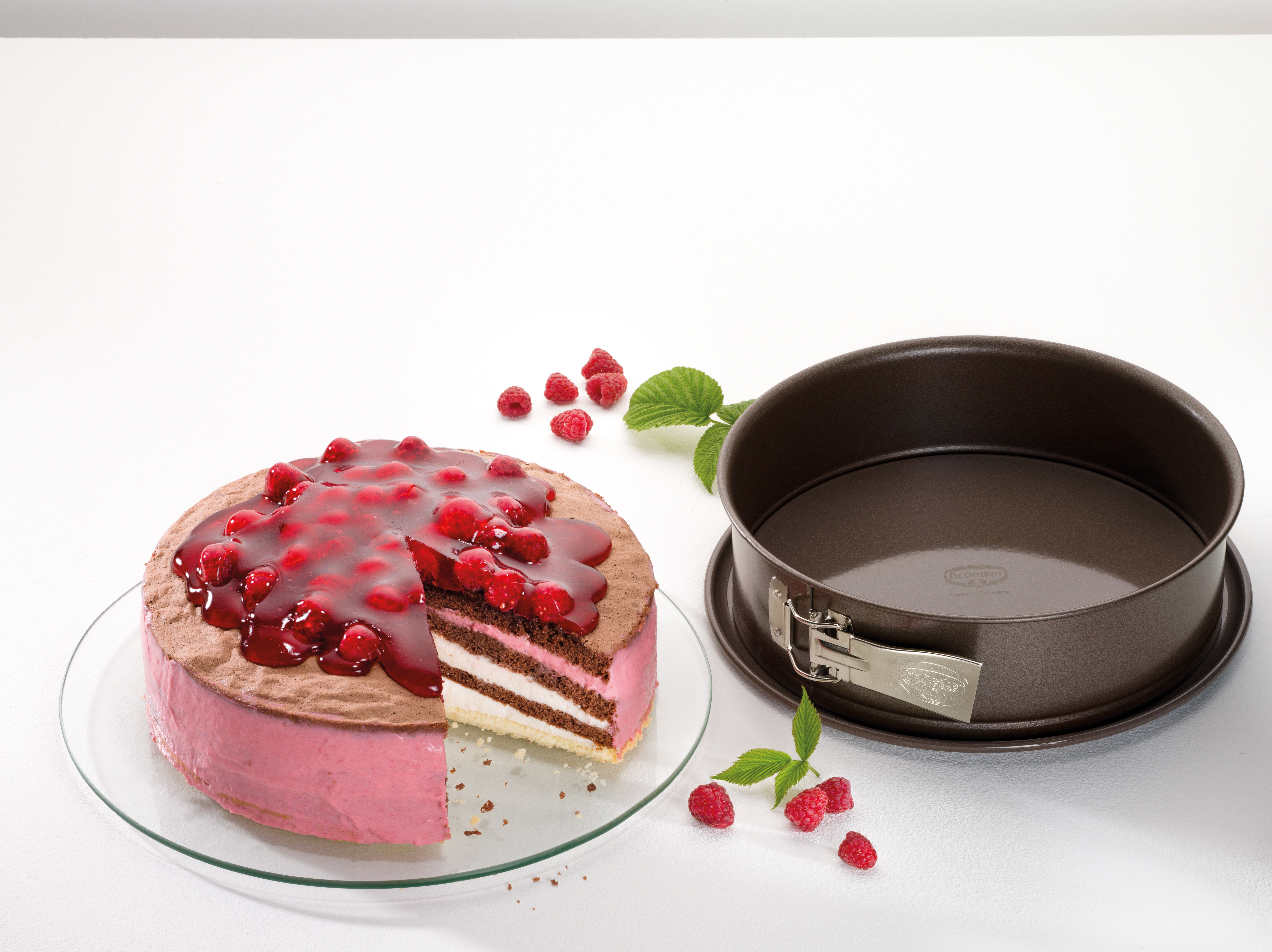 Kuchen mit rotem Fruchtbelag und einem herausgeschnittenen Stück, neben einer Backform.