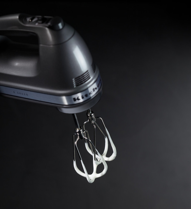 Hand mixer with beaters. White cream is visible on beaters. Black background.