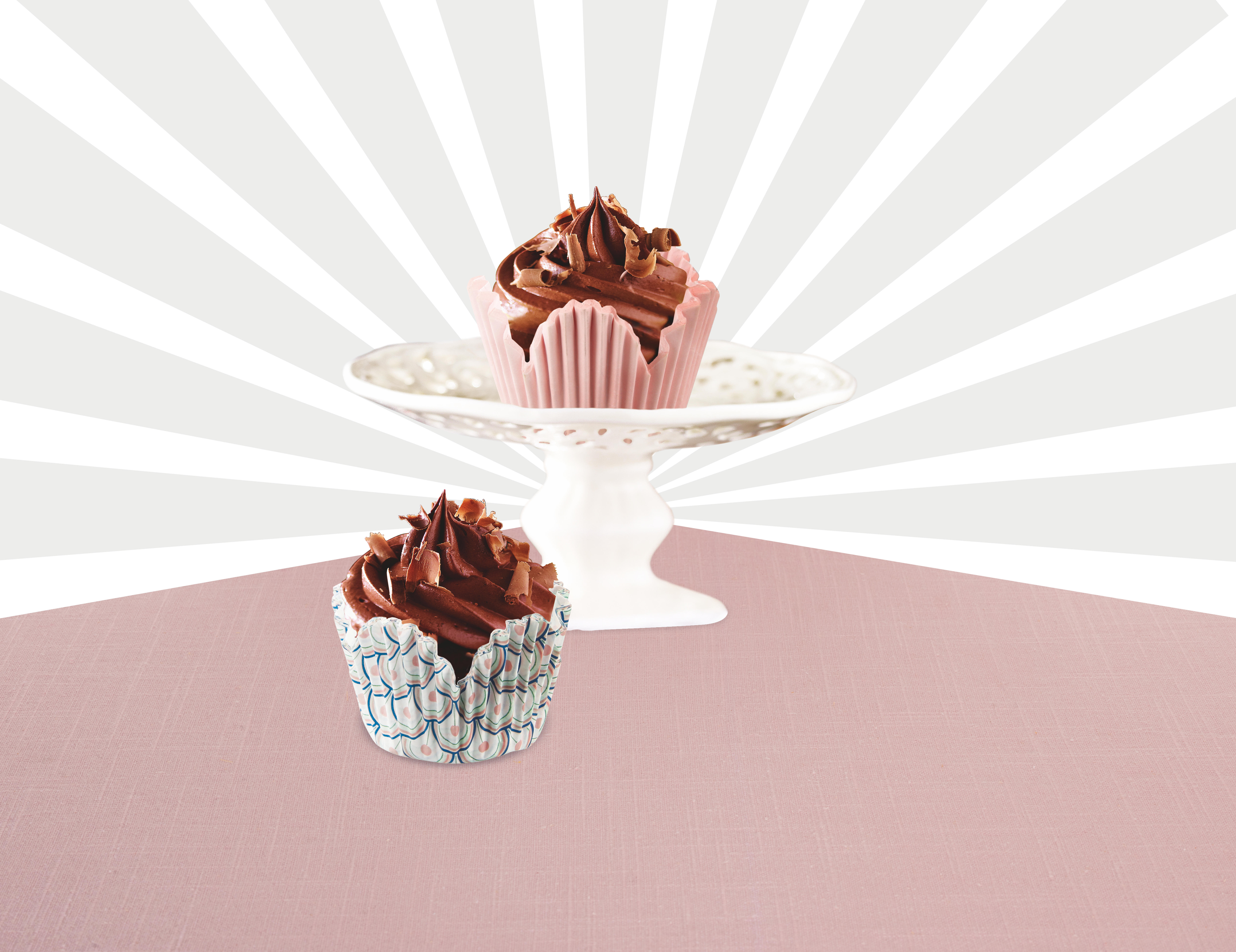 Zwei Cupcakes mit Schokoladen-Frosting auf einem Tisch. Weißer Hintergrund mit rosa Akzenten.