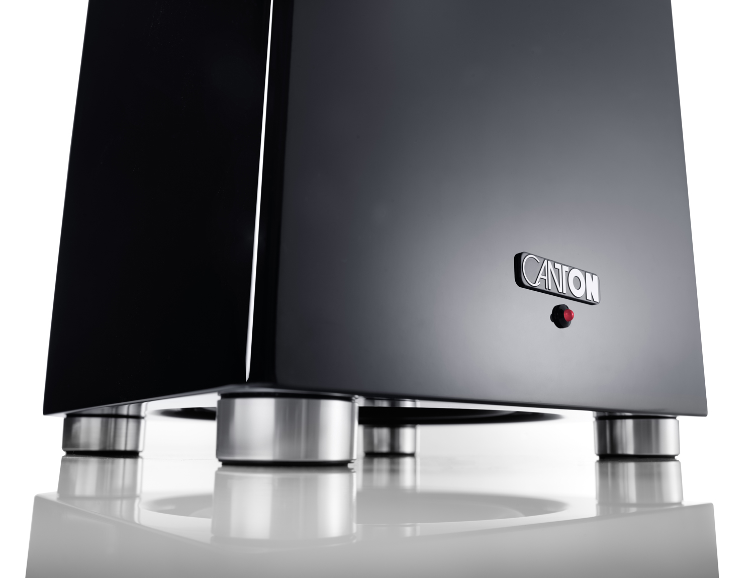 Ein schwarzer Lautsprecher mit silbernen Füßen und rotem Licht, auf weißer Oberfläche.