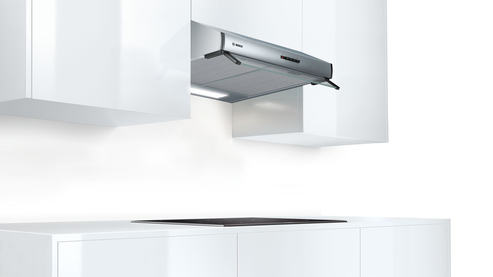 Une cuisine blanche moderne avec une hotte aspirante en acier inoxydable intégrée au-dessus d'une plaque de cuisson noire.