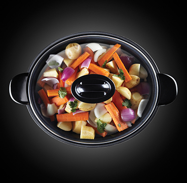 Een slowcooker met groenten erin, van bovenaf gezien, met een glazen deksel.