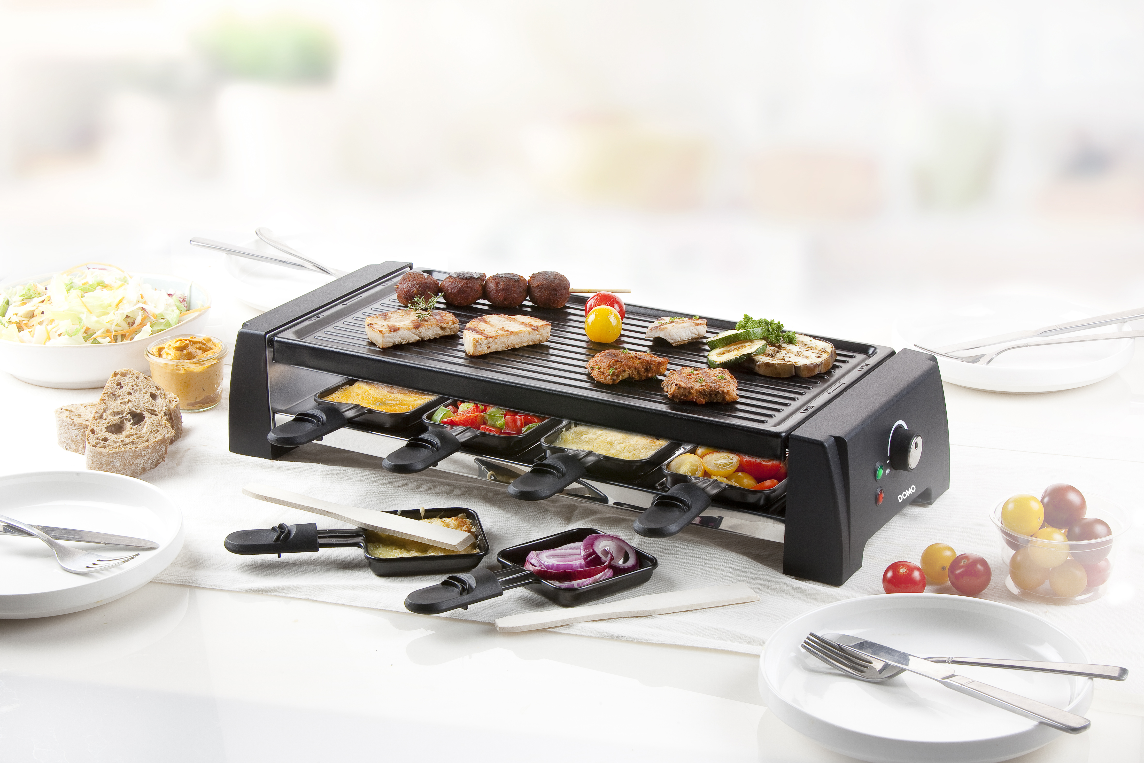 Raclette grill met eten op een tafel met borden en bestek.