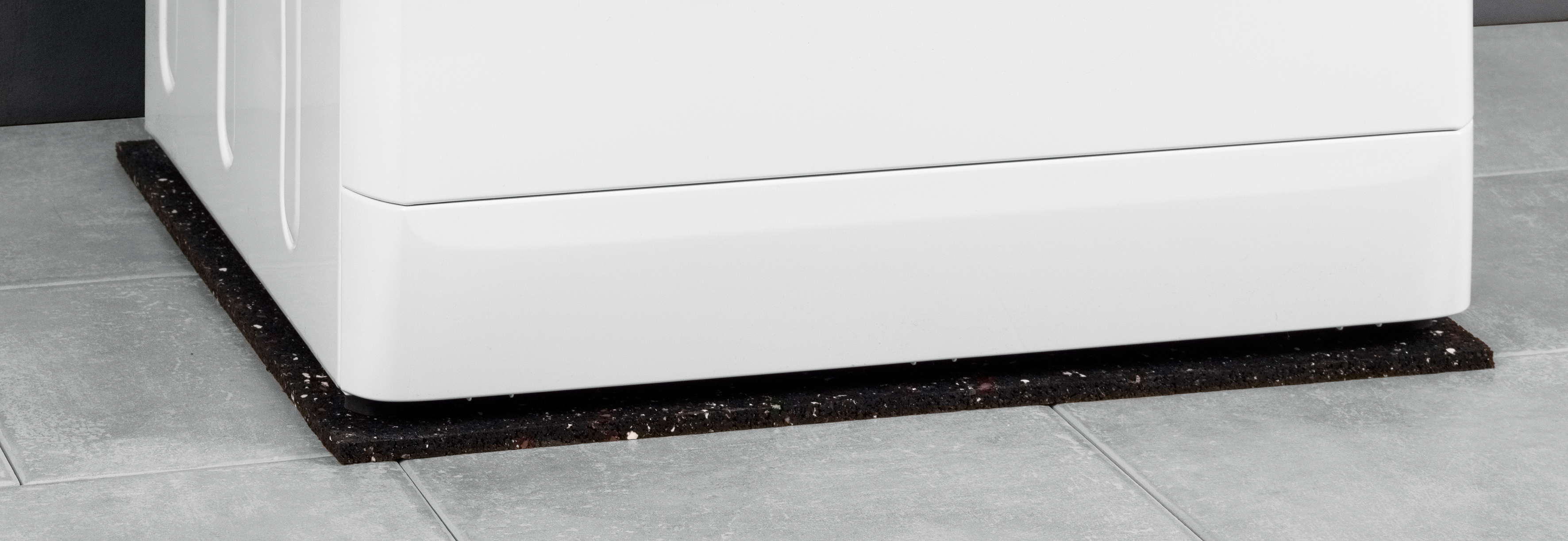 White washing machine on a black anti-vibration mat. The mat is on a tiled floor.