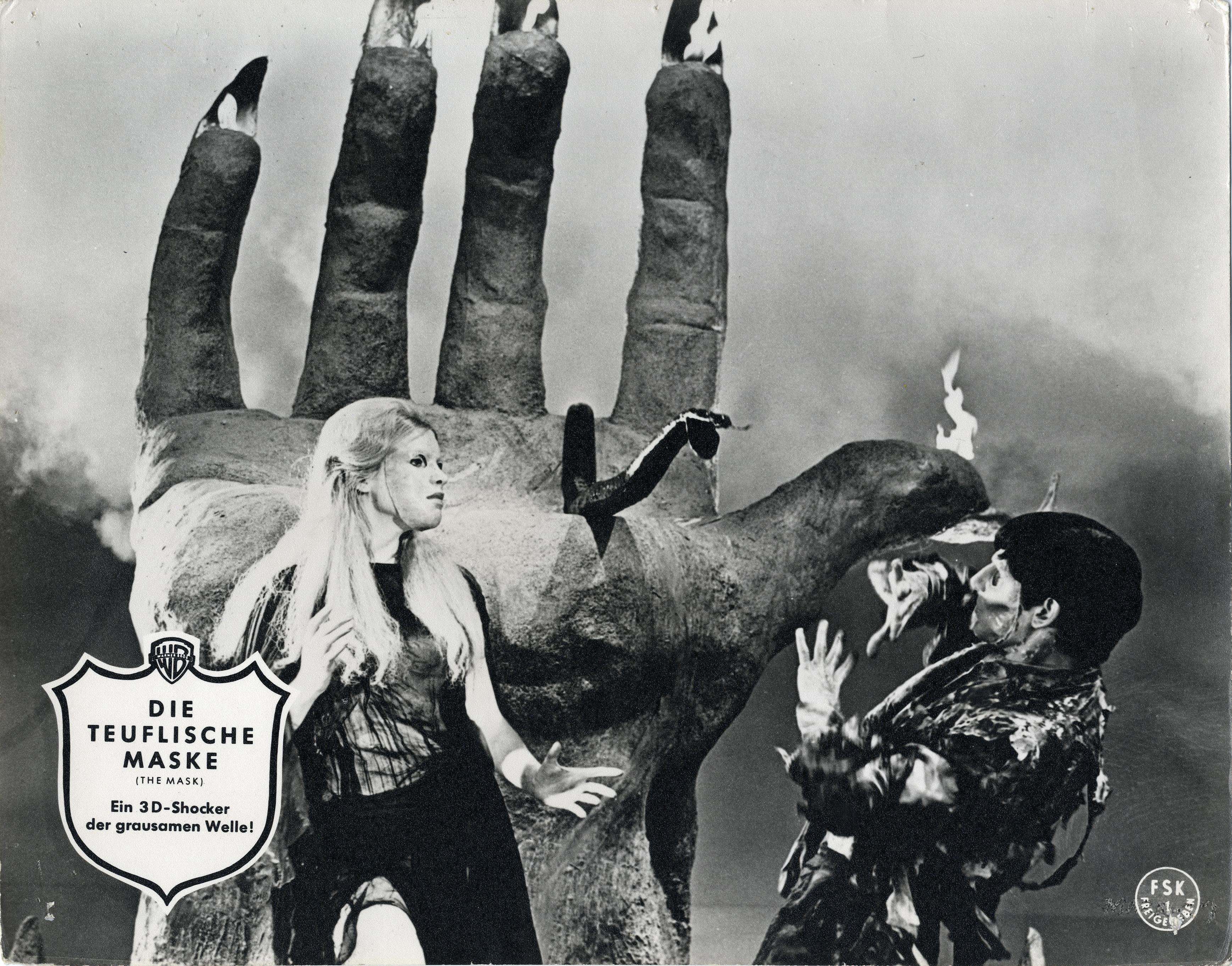 Ein Filmplakat mit einer Frau und einem Mann in der Hand eines Monsters. Schwarz-Weiß-Bild.