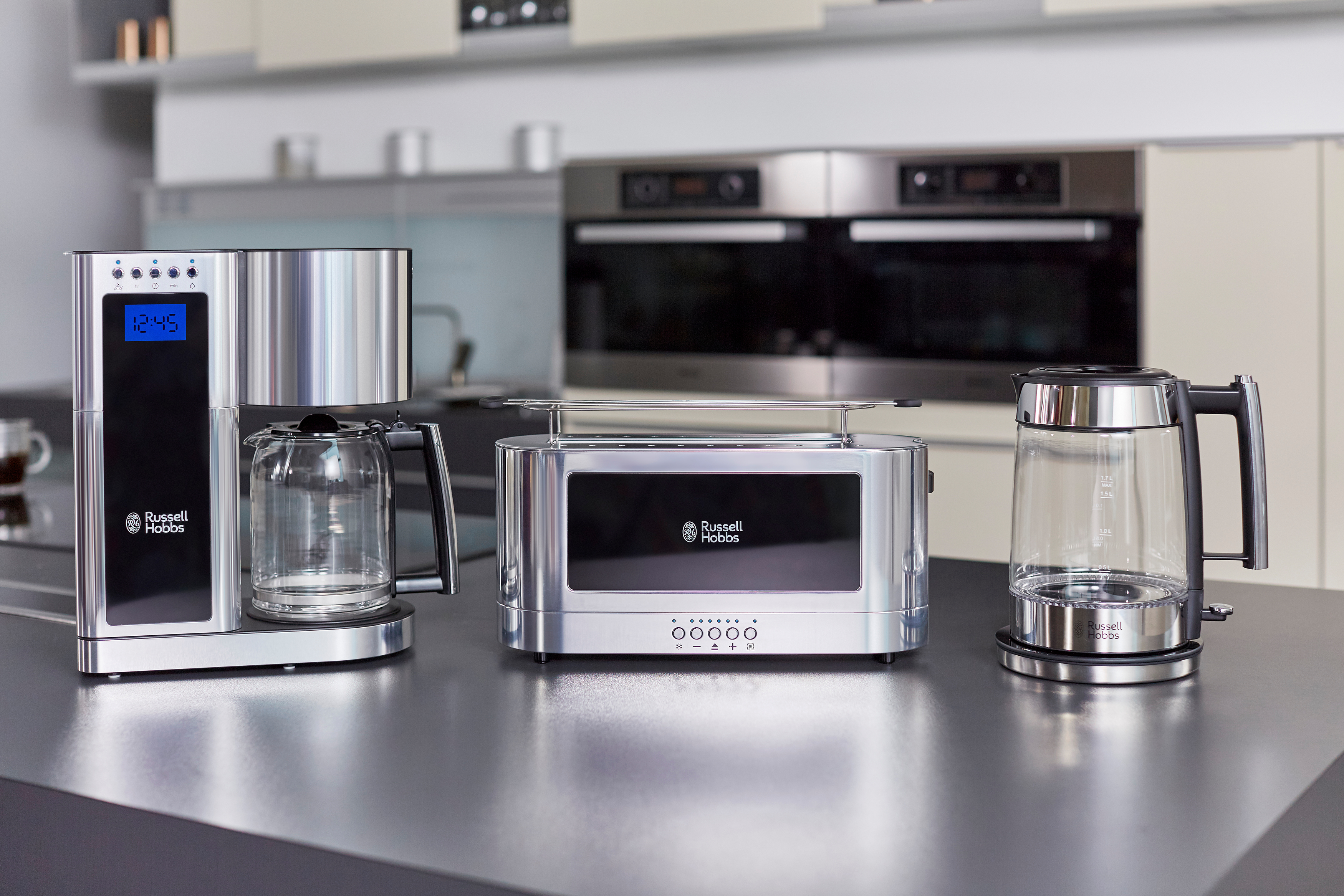 Küchengeräte: Kaffeemaschine, Toaster und Wasserkocher, alle in Silber, auf dunkler Oberfläche.