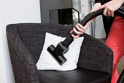 Eine Person, die ein Kissen auf einem Stuhl absaugt. Der Staubsaugeraufsatz wird verwendet.