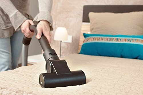 Eine Person saugt ein Bett ab. Der Staubsaugerkopf liegt auf dem Bett. Kissen liegen auf dem Bett.