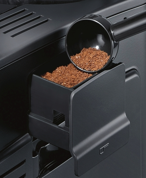 Kaffeepulver wird in eine schwarze Kaffeemaschine geschöpft.