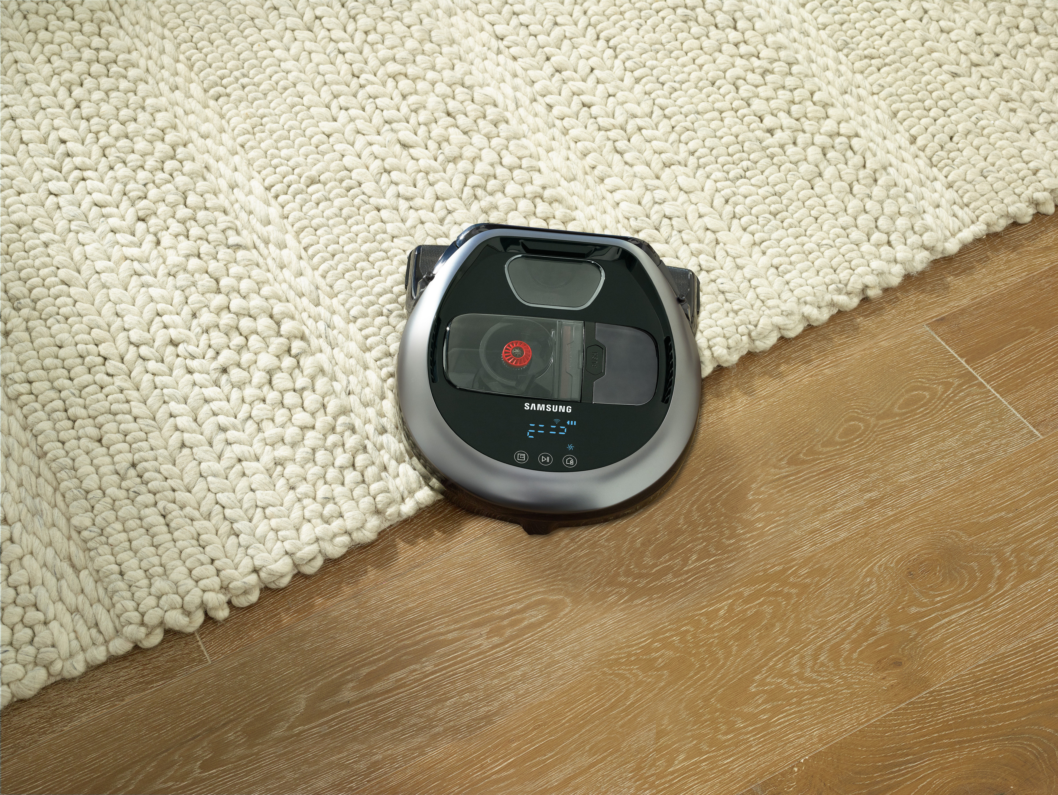 Roboter-Staubsauger auf einem Teppich und Boden. Der Staubsauger ist grau.
